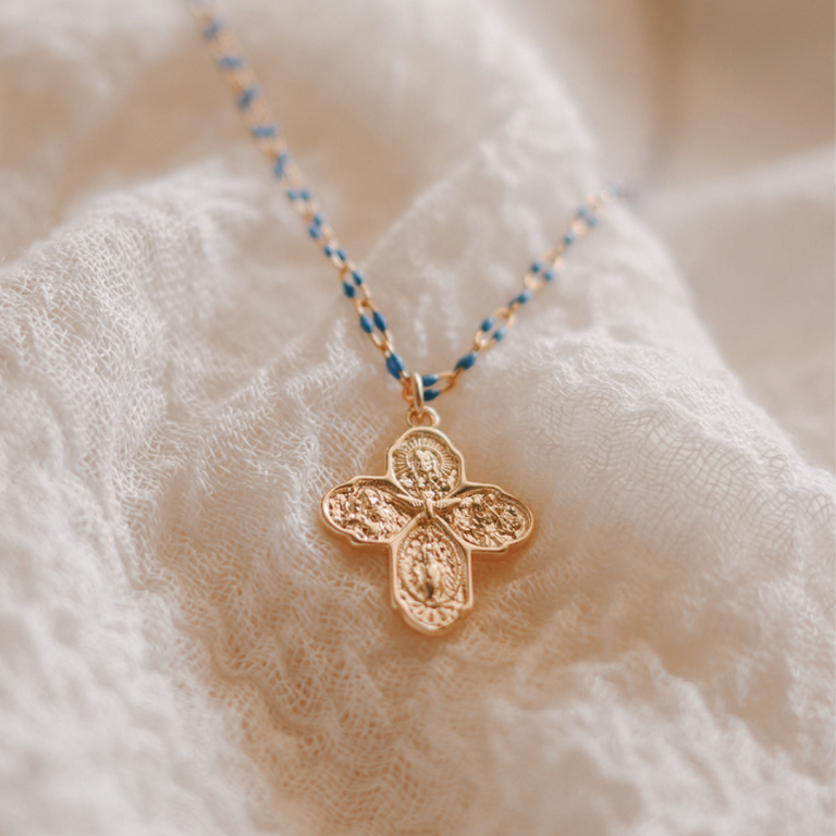 Gold four-way cross pendant on blue beaded chain necklace.