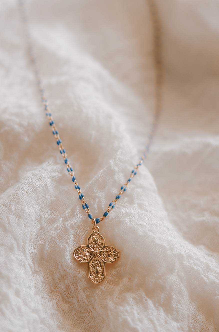 Gold four-way cross pendant on blue beaded chain necklace.