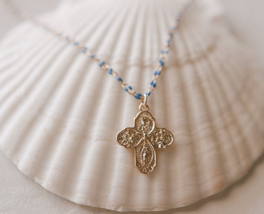 Gold four-way cross pendant on blue beaded chain necklace close-up.