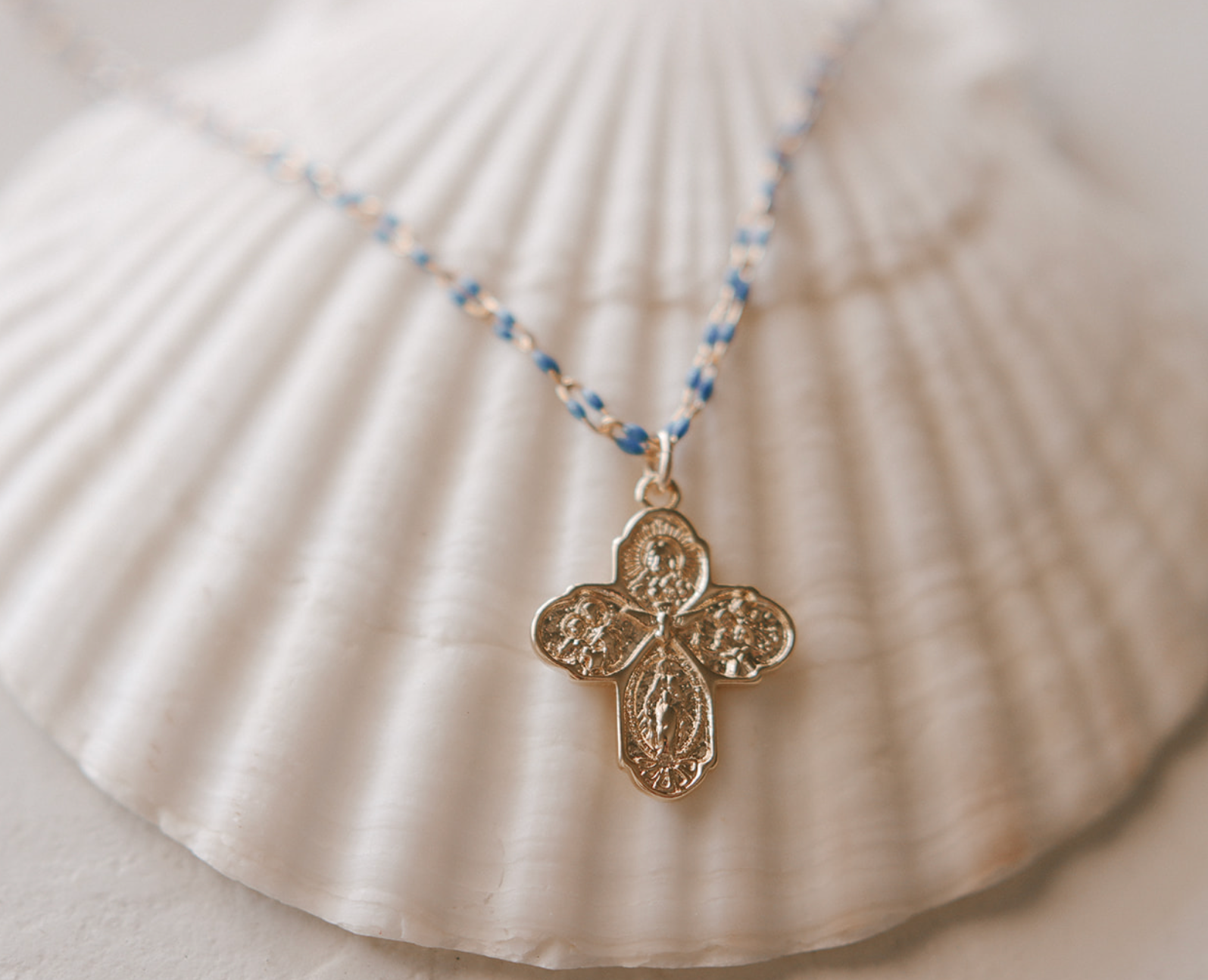 Gold four-way cross pendant on blue beaded chain necklace close-up.