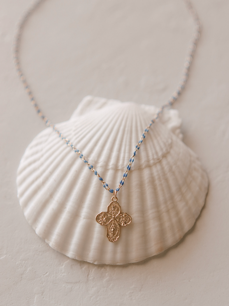 Gold four-way cross pendant necklace with blue beaded chain on white pouch.