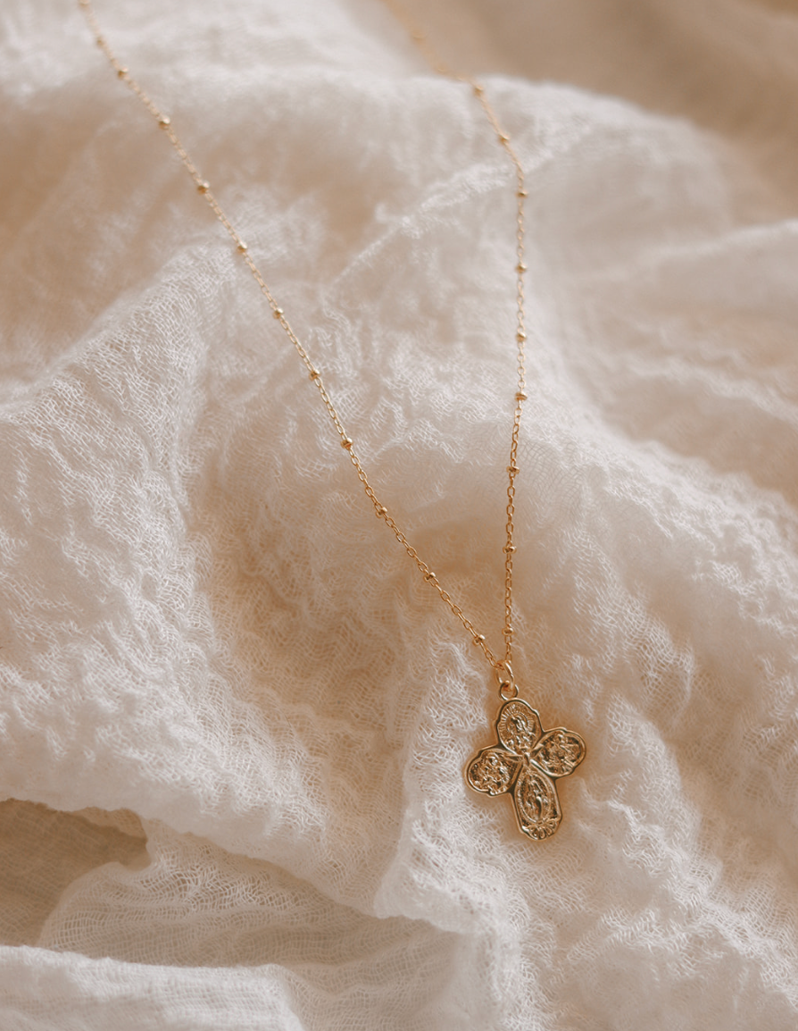 Gold cross necklace with ornate filigree cross pendant on a thin chain