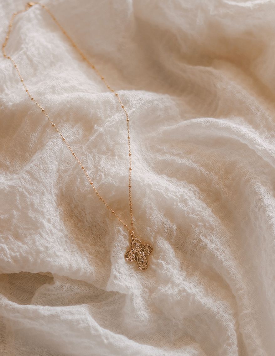 Gold cross necklace with ornate filigree pendant on a thin chain