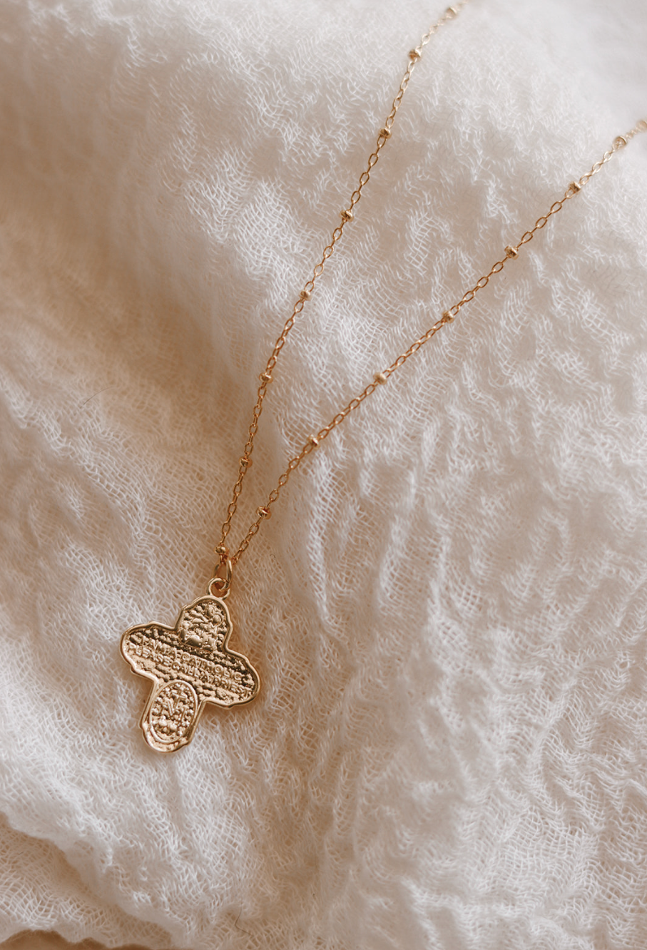 Gold-tone cross pendant necklace with delicate chain, close-up on pendant.