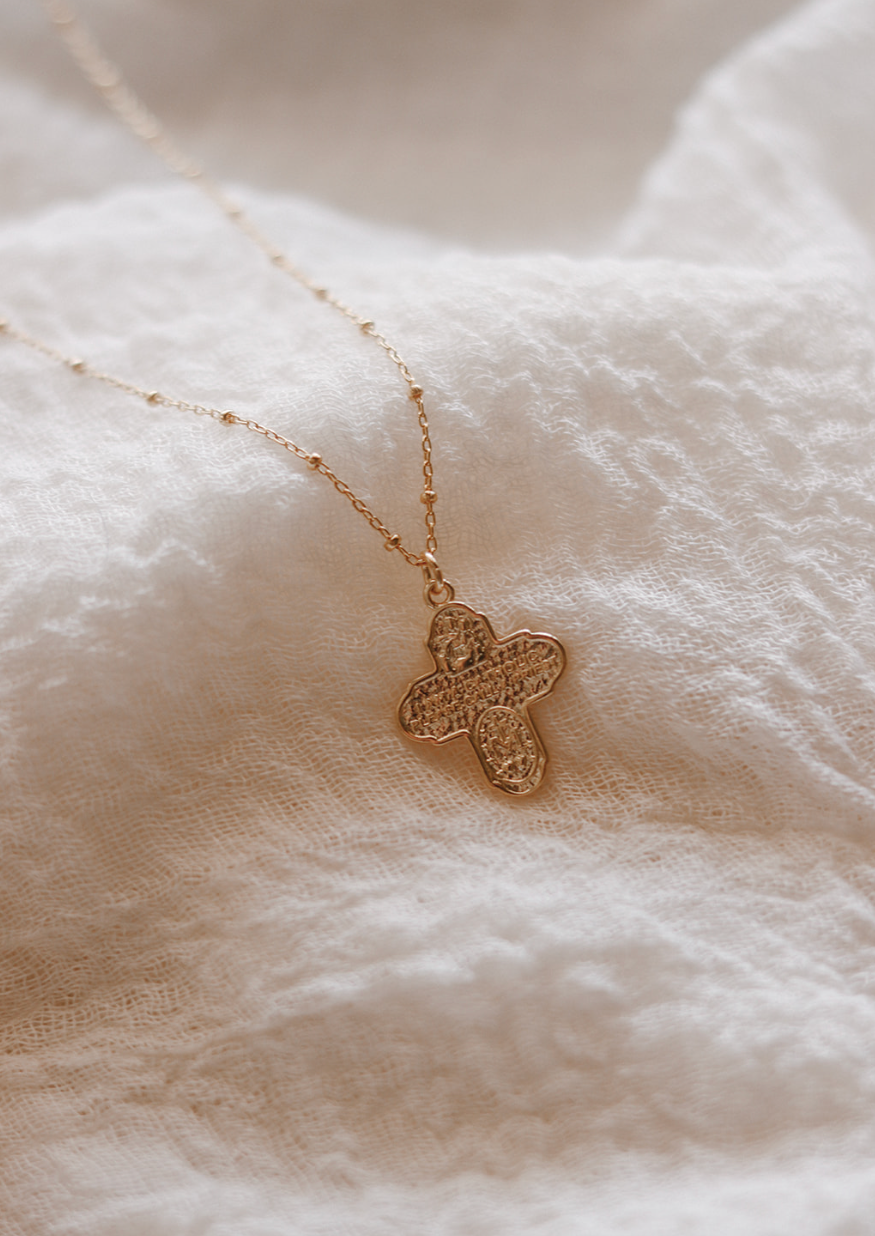 Gold-tone cross pendant necklace with delicate chain, pendant at center.