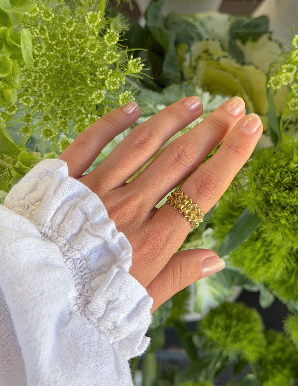 Gold-tone textured ring with raised shield pattern on finger