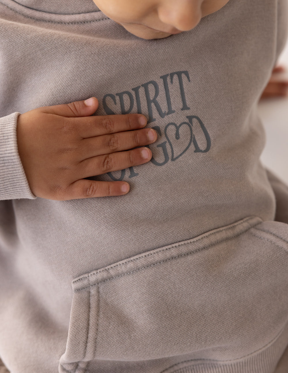 Kids taupe hoodie close-up: “SPIRIT OF GOD” chest print and front pouch pocket