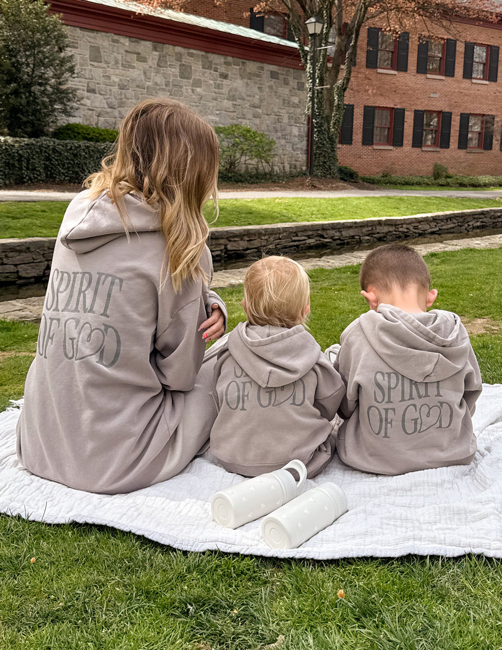 Kids taupe hoodies with “SPIRIT OF GOD” back graphics, worn while sitting outdoors