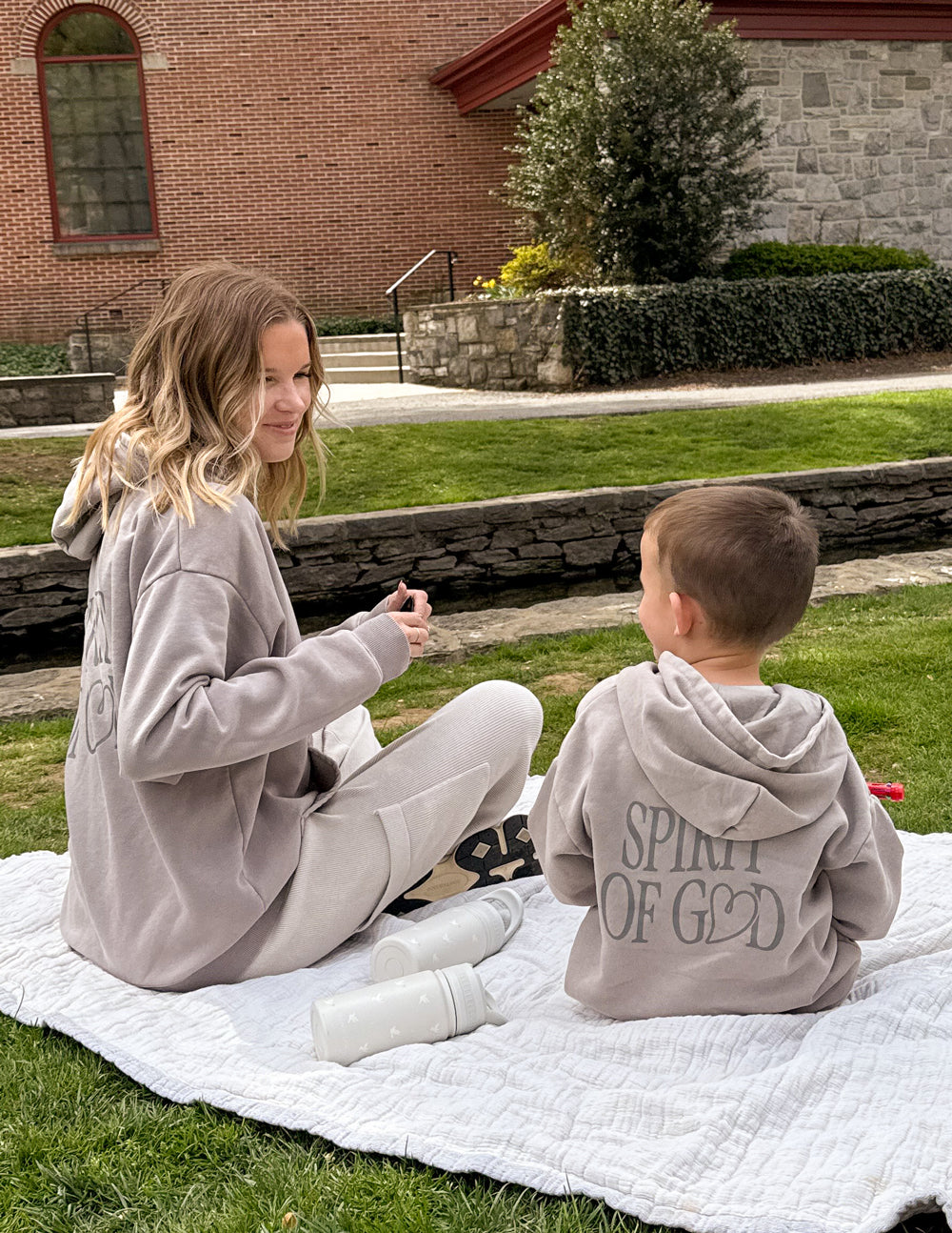 Kids taupe hoodie with hood and “SPIRIT OF GOD” back print, child sitting outdoors