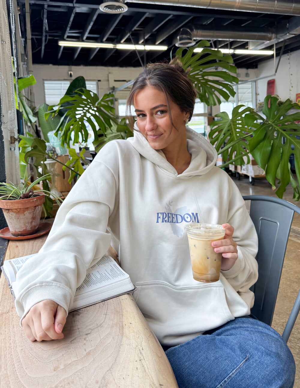 Cream unisex hoodie with blue "FREEDOM" chest print, front view while seated