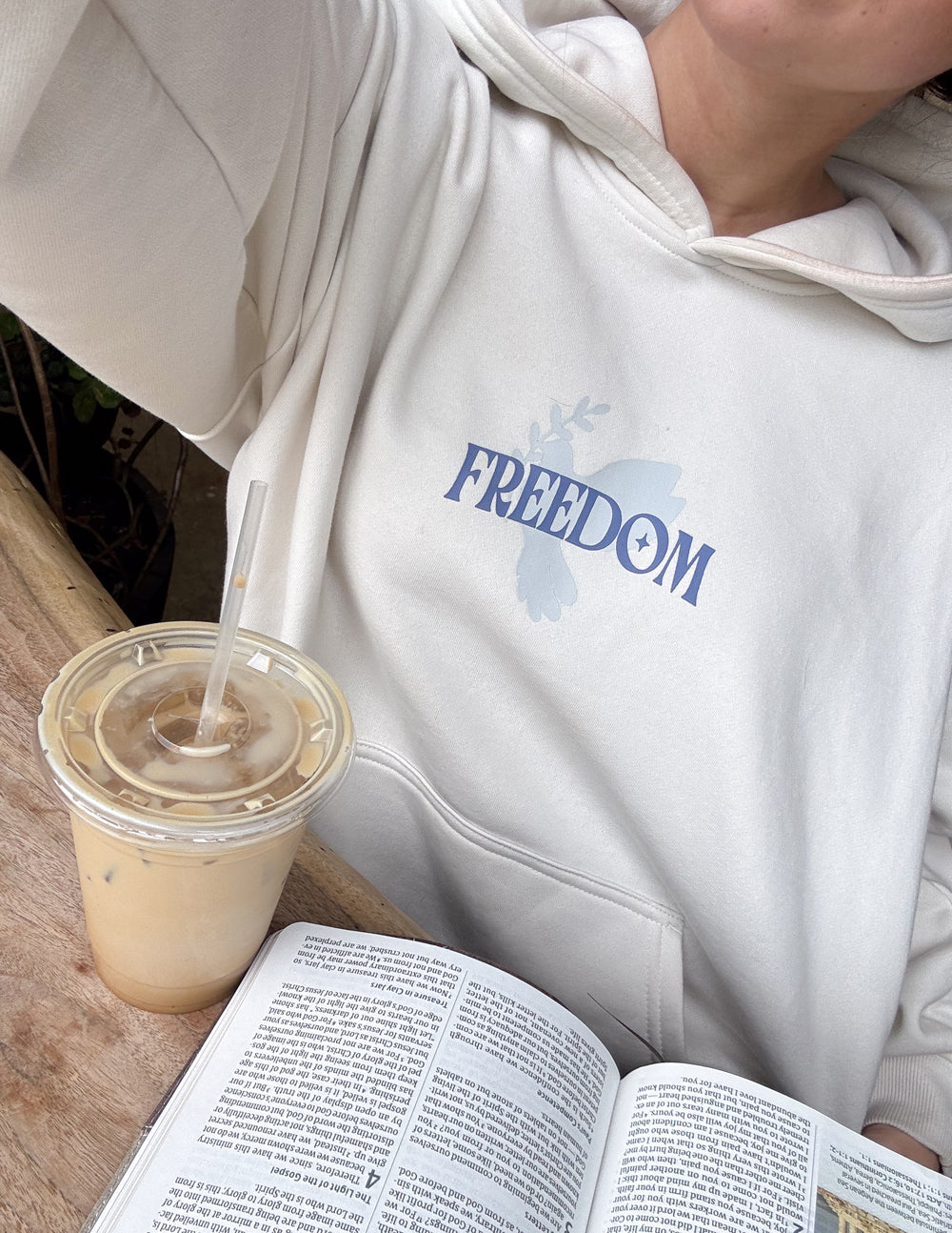 White unisex hoodie close-up with blue 'Freedom' logo on chest and drawstring hood.