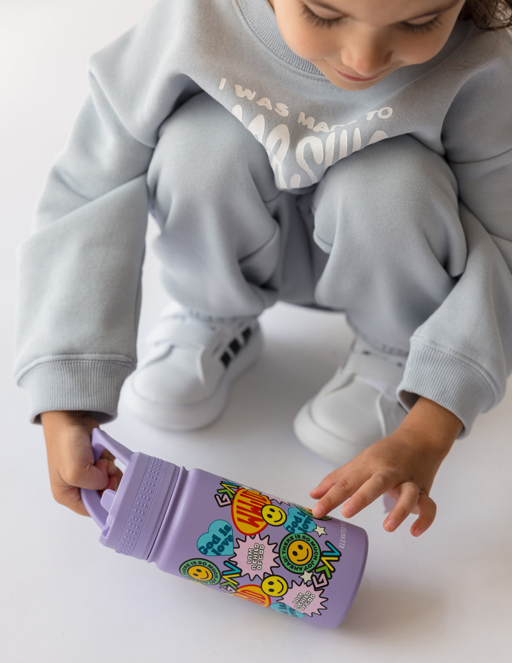 Lavender kids water bottle with sticker collage, held by child’s hands