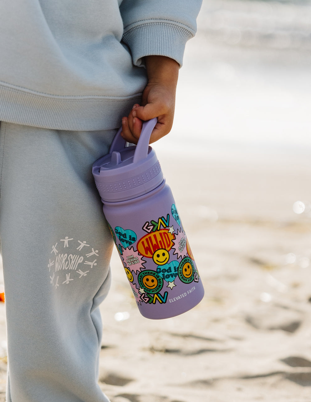 Lavender kids water bottle with sticker collage graphic and flip spout, outdoors