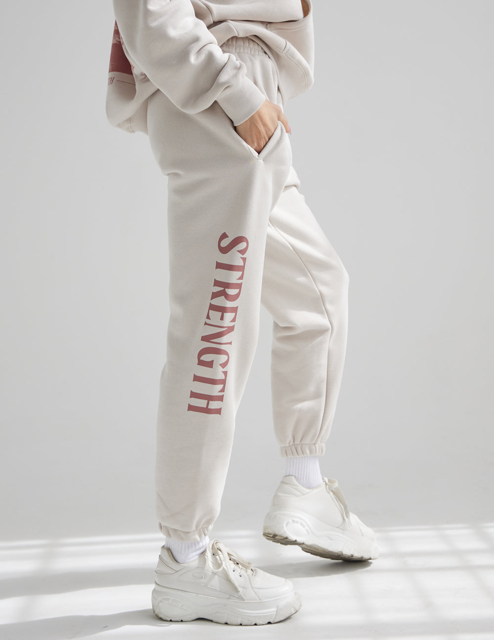 Cream unisex sweatpants with red STRENGTH vertical print, gathered ankle cuffs and drawcord