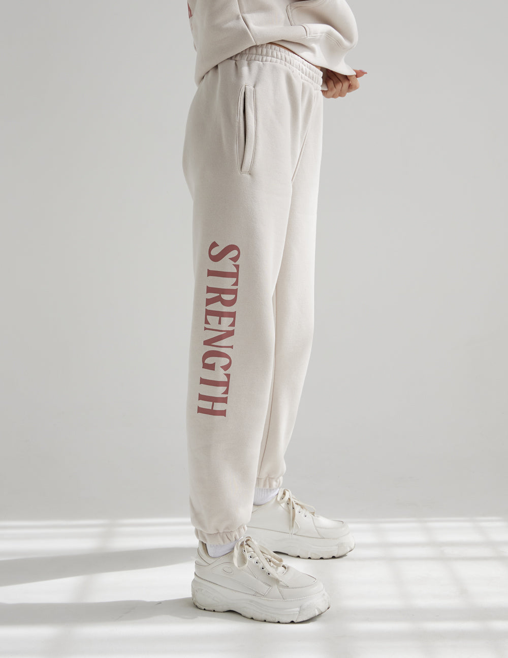 Cream unisex sweatpants with red STRENGTH leg print, drawstring waistband and ankle cuffs