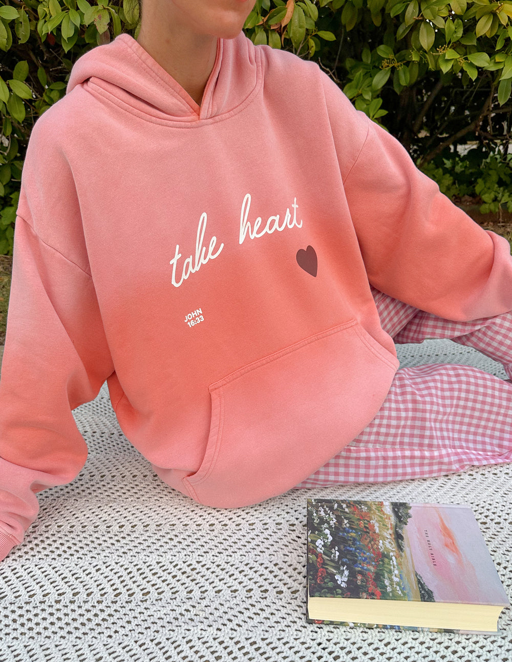Pink unisex hoodie close-up with 'take heart' script, heart graphic, kangaroo pocket