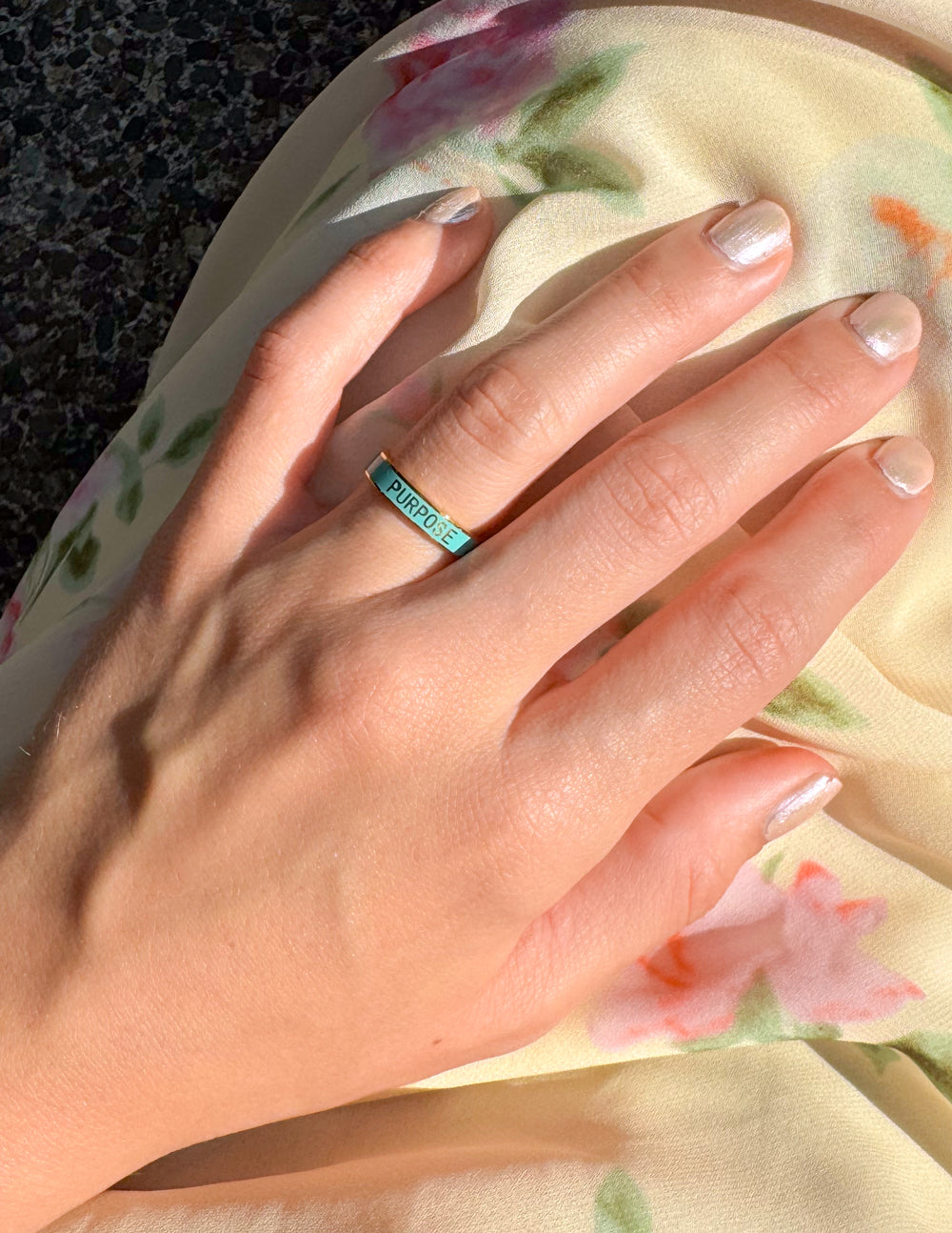 Teal enamel ring on hand, gold band with “PURPOSE” engraving