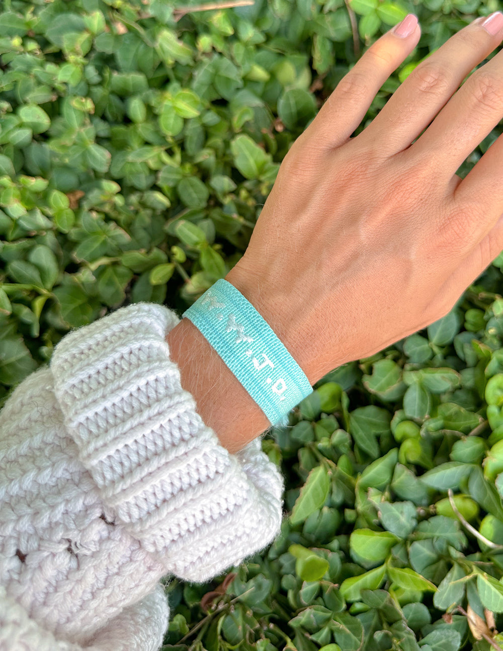Light teal embroidered bracelet on wrist with braided texture and tassels