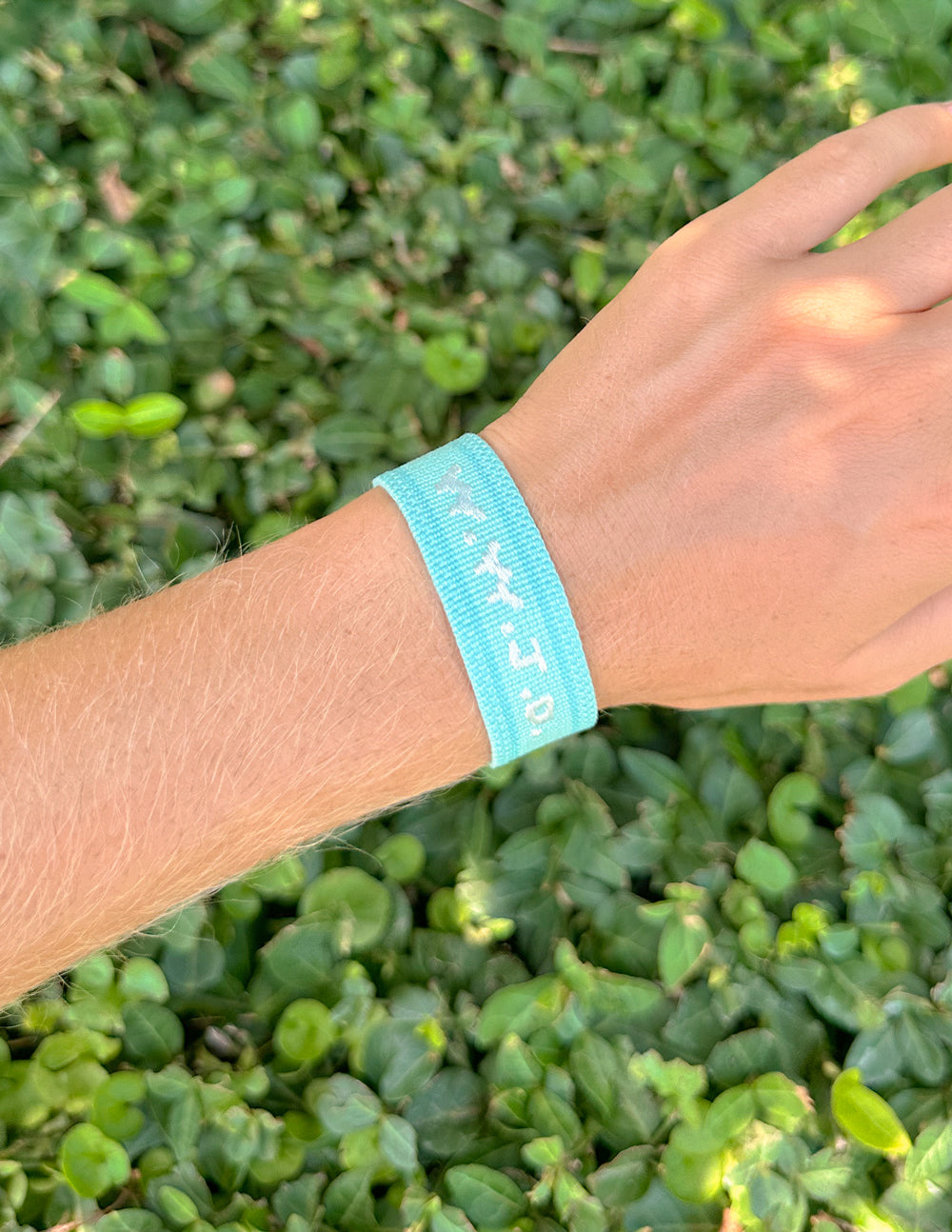 Light teal embroidered bracelet on wrist with stitched WWJD pattern and tassels