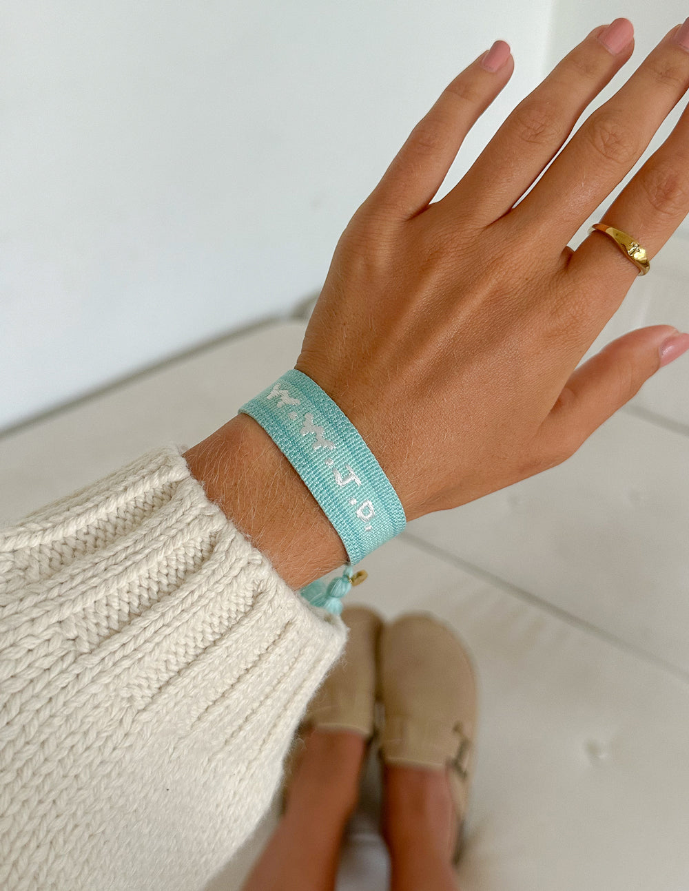 Light teal embroidered bracelet on wrist with braided strap, tassels, and charm