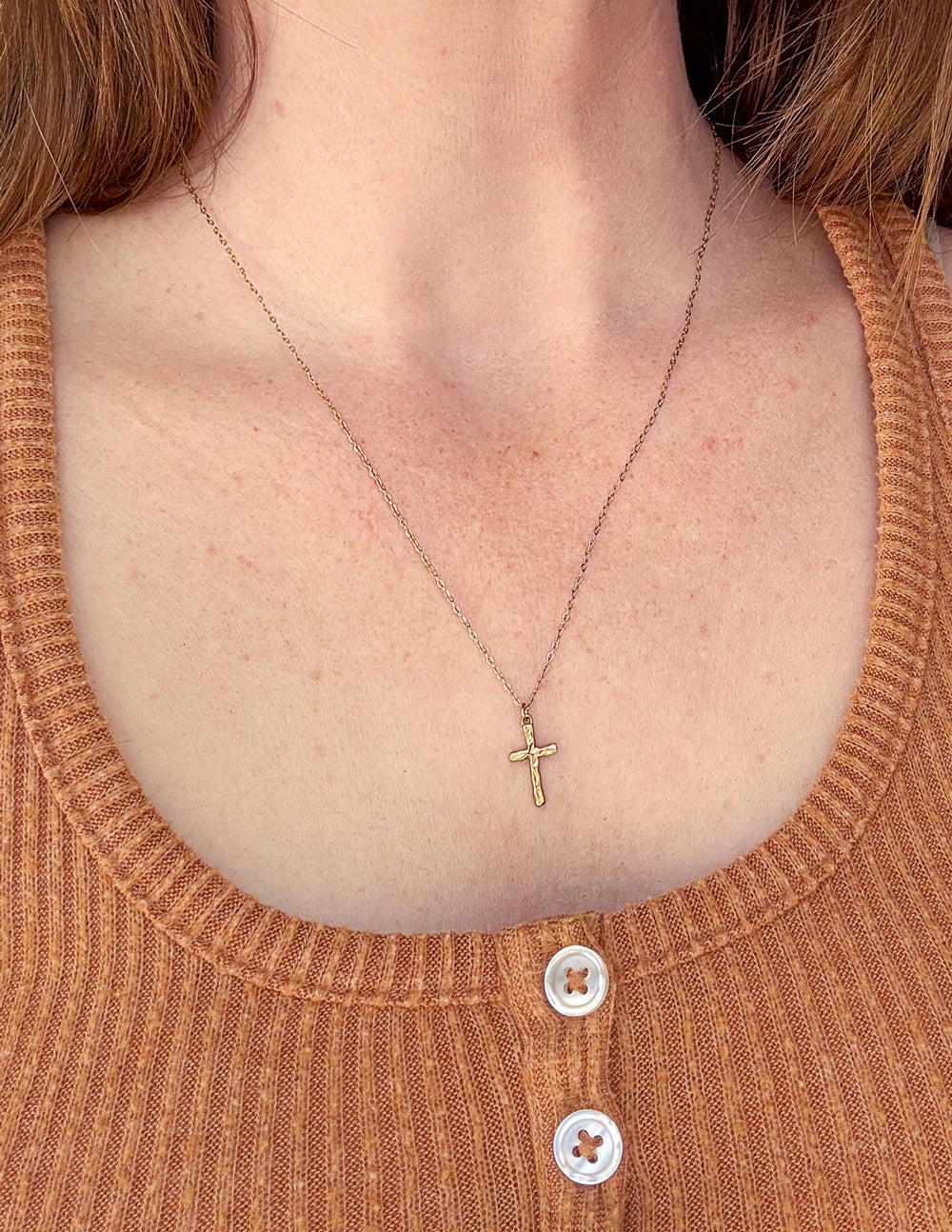 Gold cross pendant necklace with thin chain, worn at collar