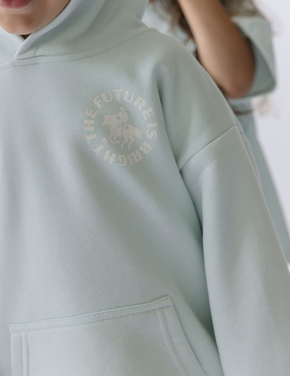 Light mint kids hoodie close-up with chest graphic and kangaroo pocket