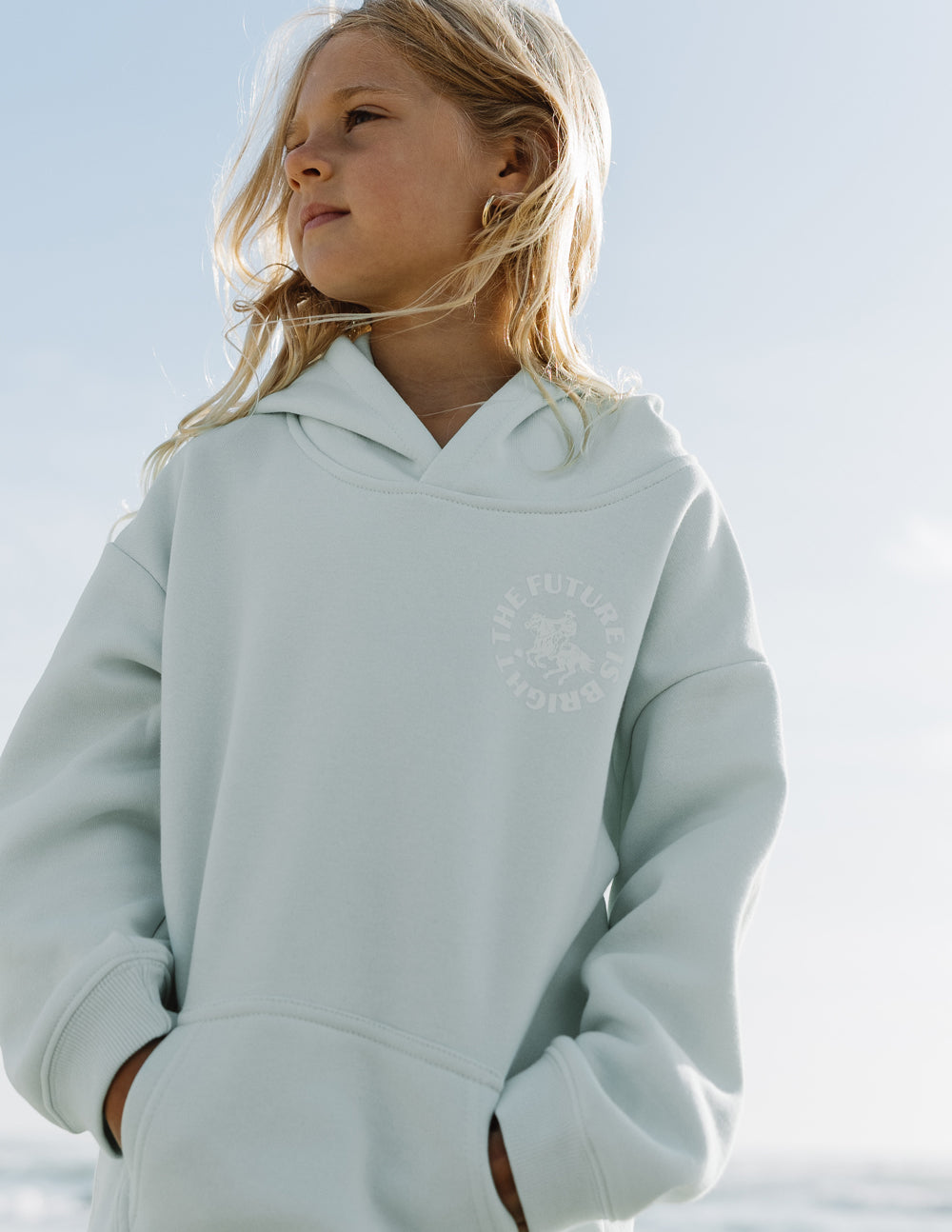Light mint kids hoodie with hood and small chest graphic, shown from side