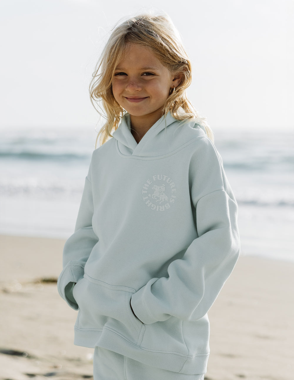 Light mint kids hoodie with hood and circular chest graphic, front pocket visible