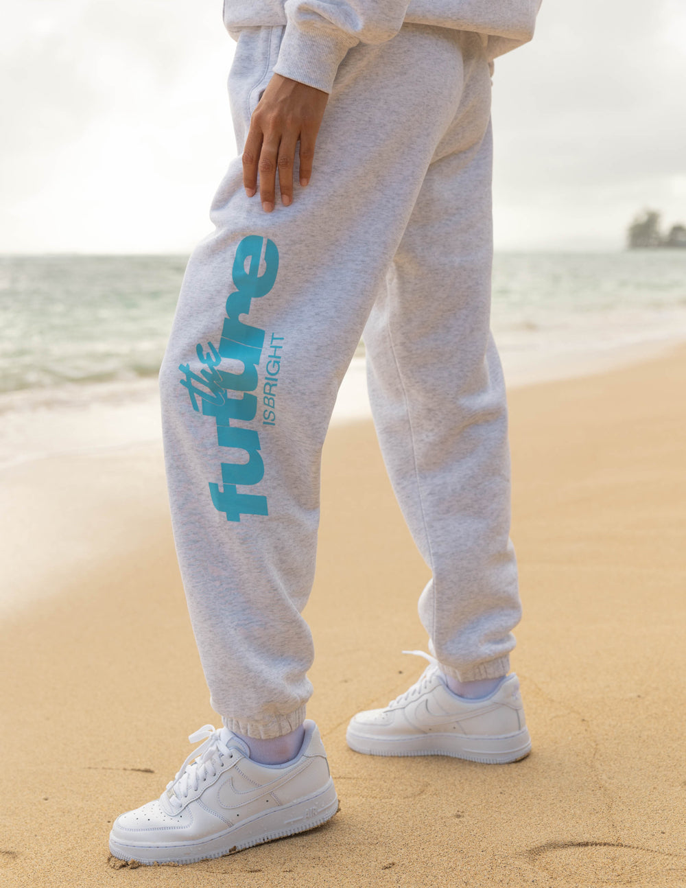 Light gray unisex sweatpants with teal logo print on left leg