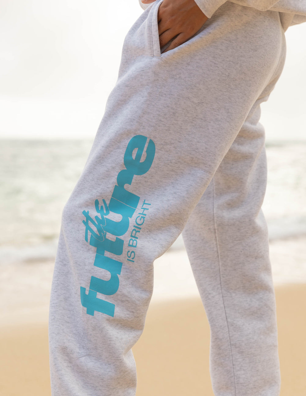 Light gray unisex sweatpants with teal logo print on side near thigh