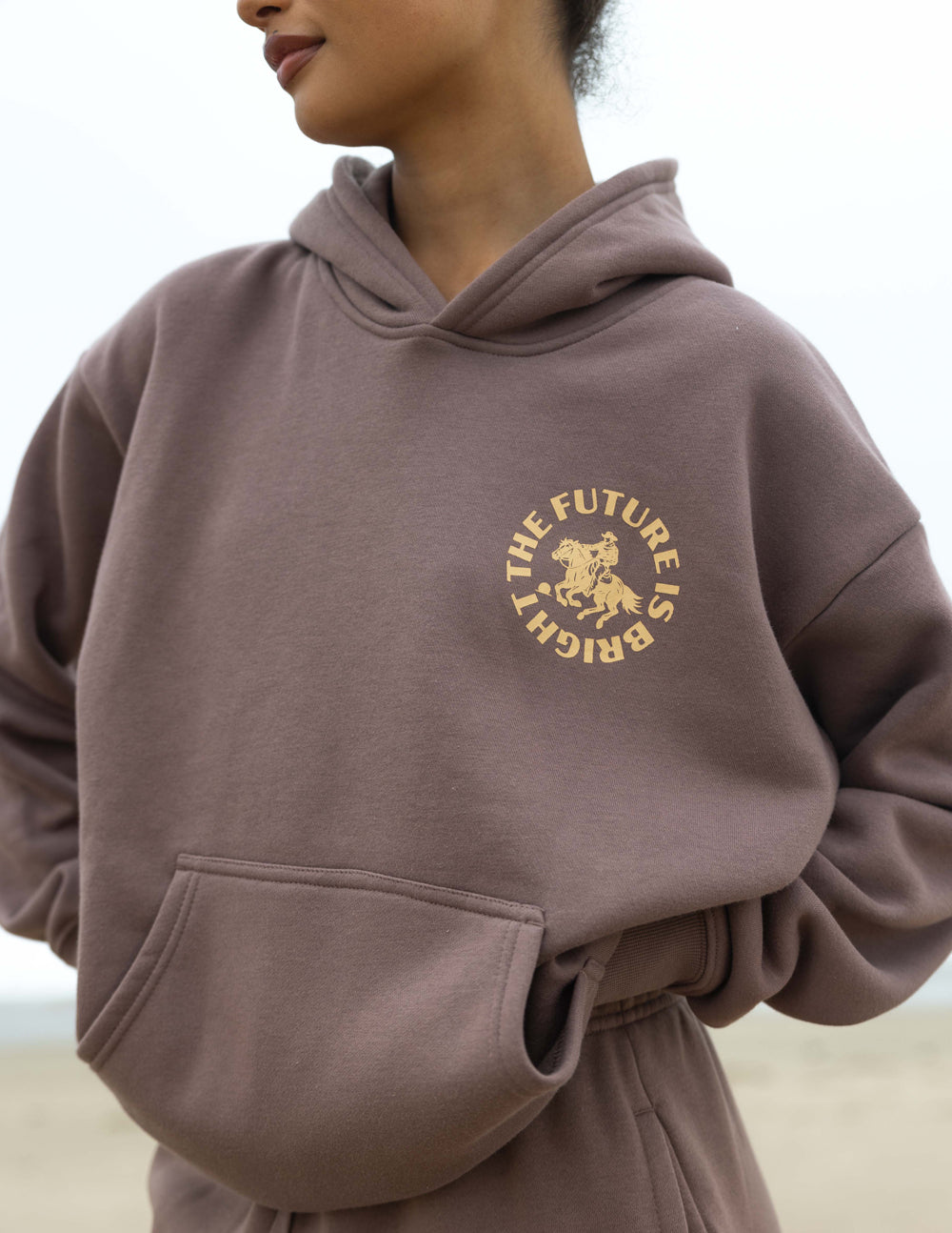 Mauve unisex hoodie with hood and gold rodeo logo at center chest.