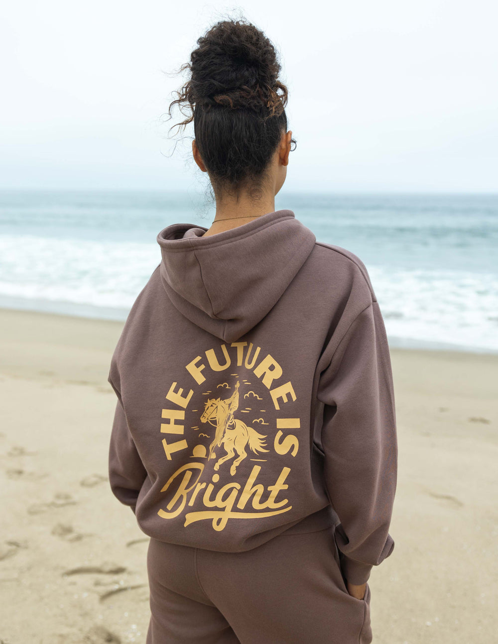 Mauve unisex hoodie with hood and large gold rodeo graphic on back.