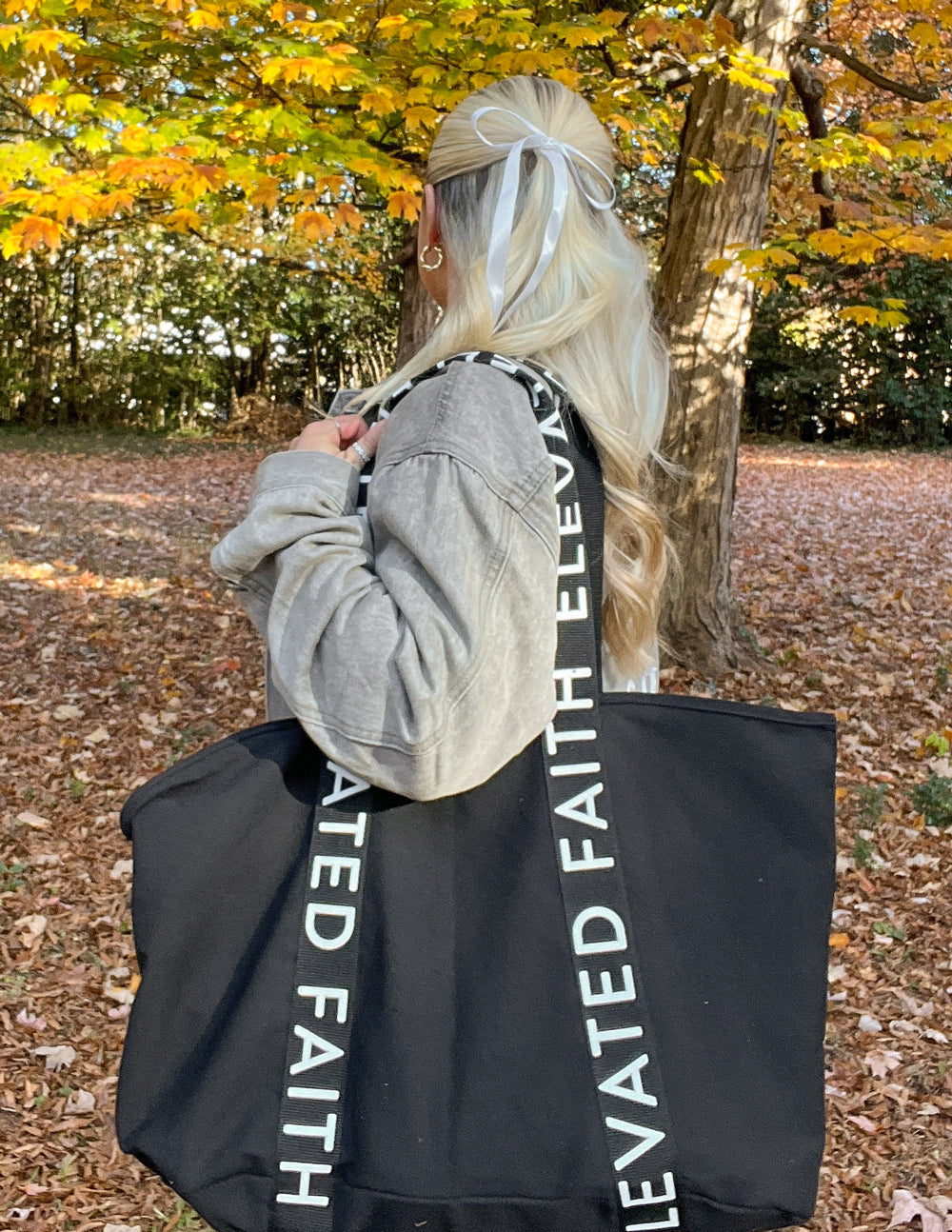 Black large tote bag viewed from the back with “ELEVATED FAITH” printed on handles