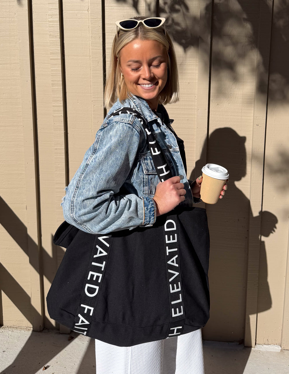 Black large tote bag with wide handles and “ELEVATED FAITH” printed strap detailing
