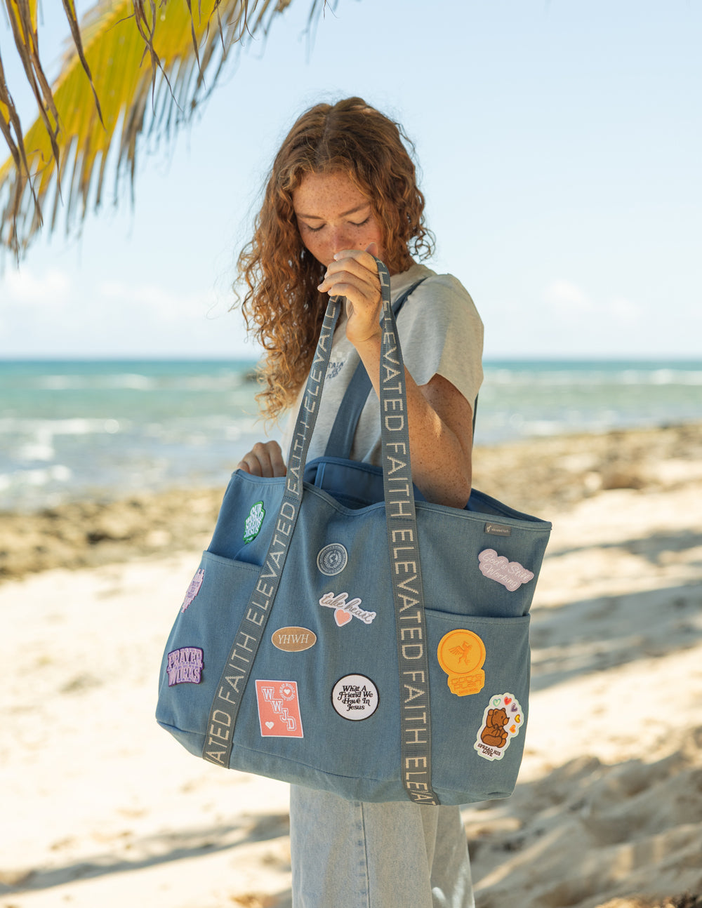 Blue denim tote bag with embroidered patches and ELEVATED FAITH webbing straps