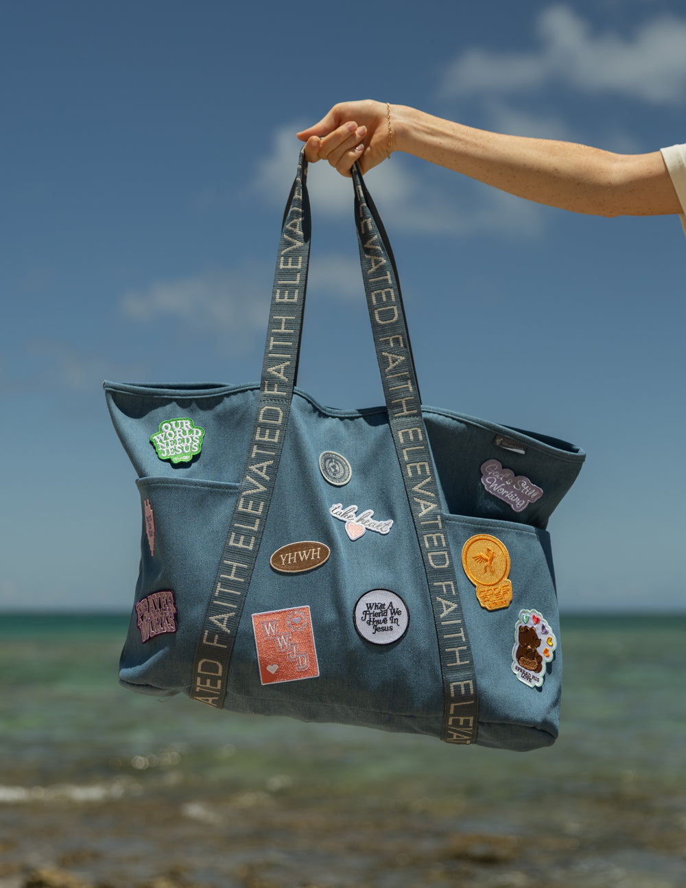 Blue denim tote bag held up with ELEVATED FAITH webbing straps and patches