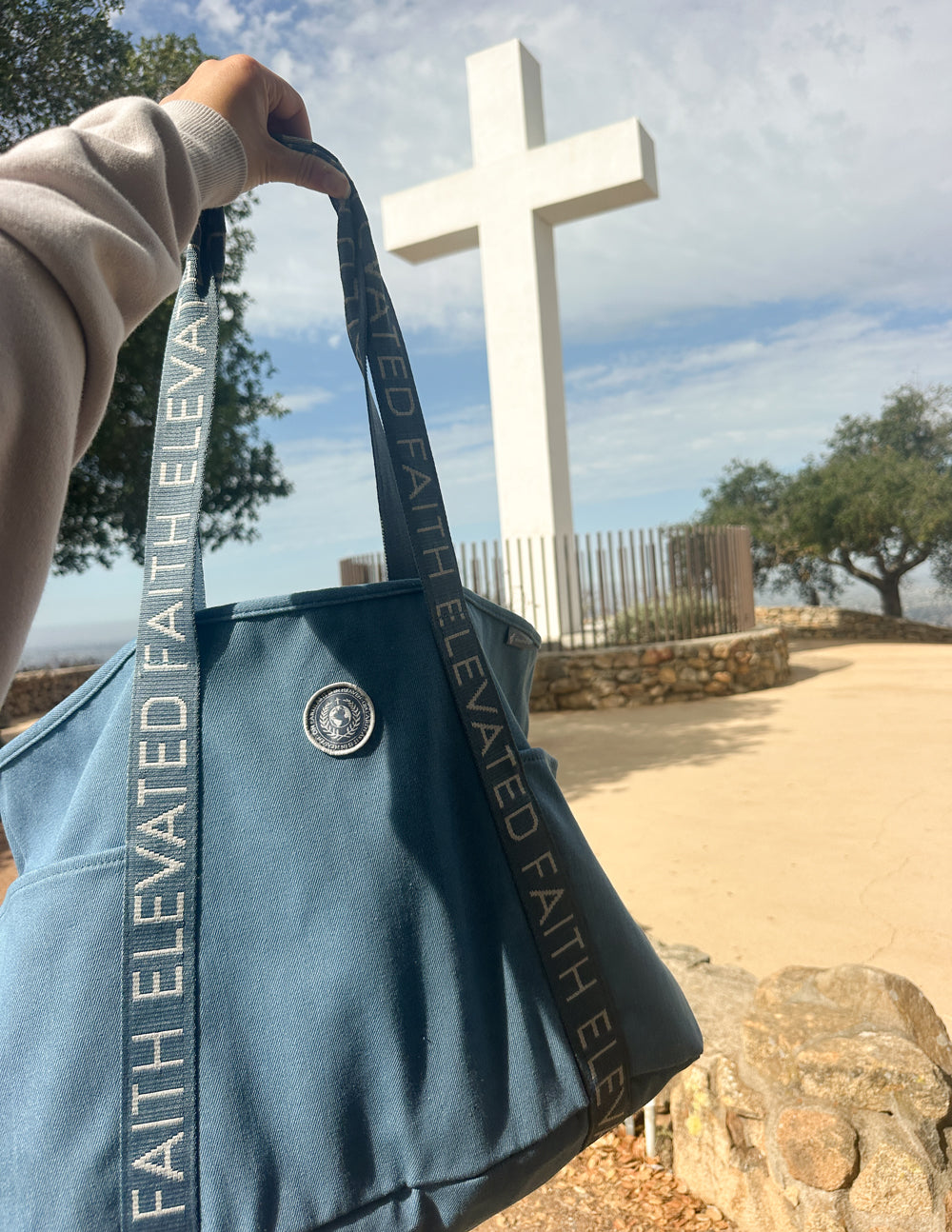 Blue denim tote bag with circular logo patch and ELEVATED FAITH webbing straps