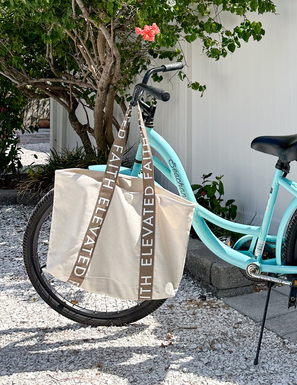 White canvas tote with brown webbing handles and vertical turquoise 'ELEVATED FAITH' text