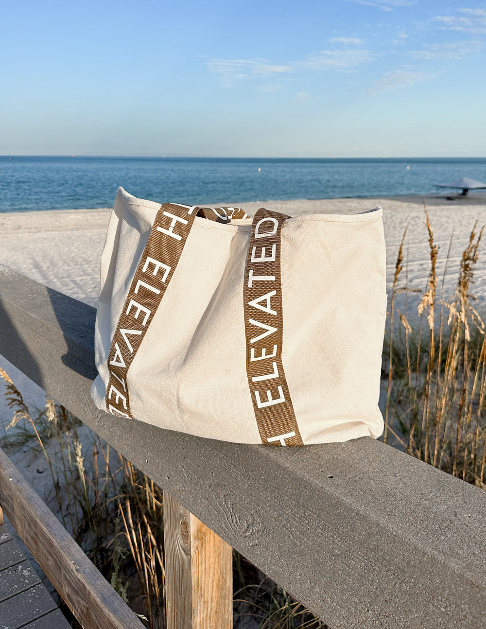 Large everyday tote on seaside fence, cream canvas and brown vertical logo straps