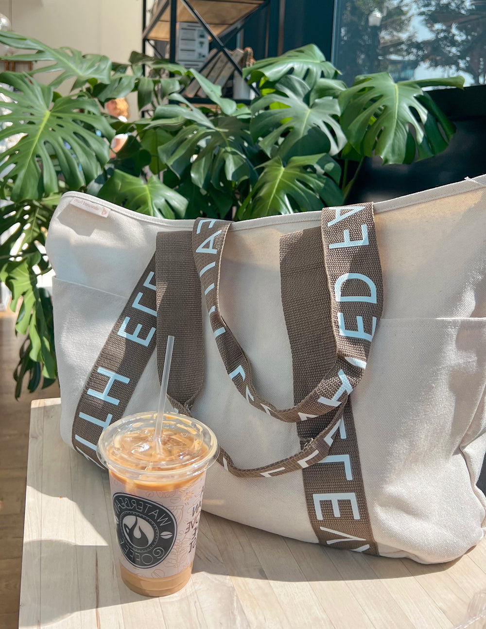 Large everyday tote with open top, cream canvas and brown logo straps, side view