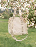 Cream mini tote bag with “ELEVATED FAITH” ribbon handles and gold-tone hardware