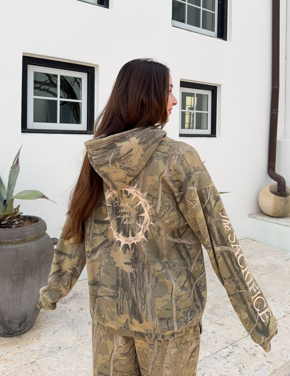 Camouflage unisex hoodie with back circular graphic and “Sacrifice” sleeve lettering