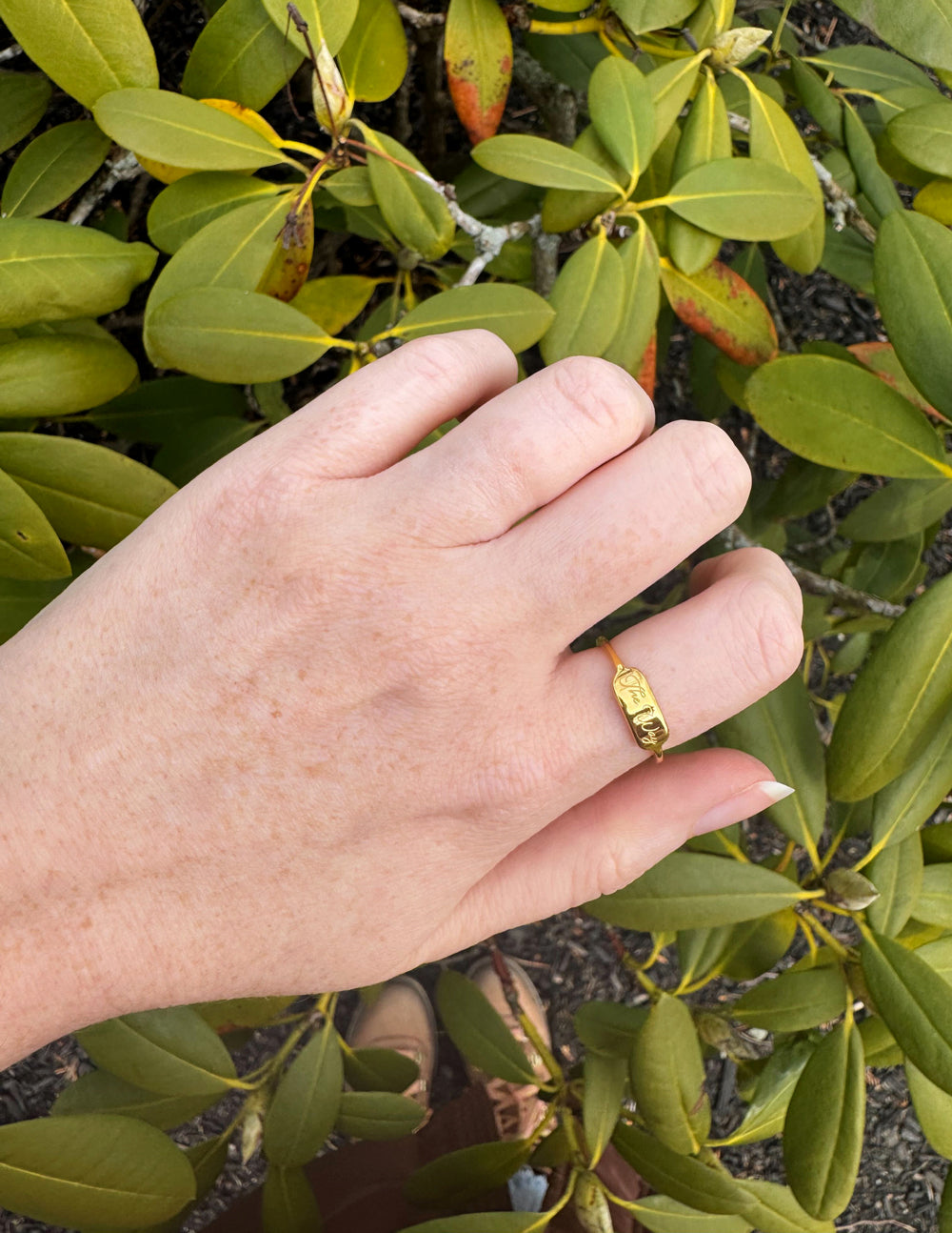 Gold tone signet ring on finger, engraved front visible