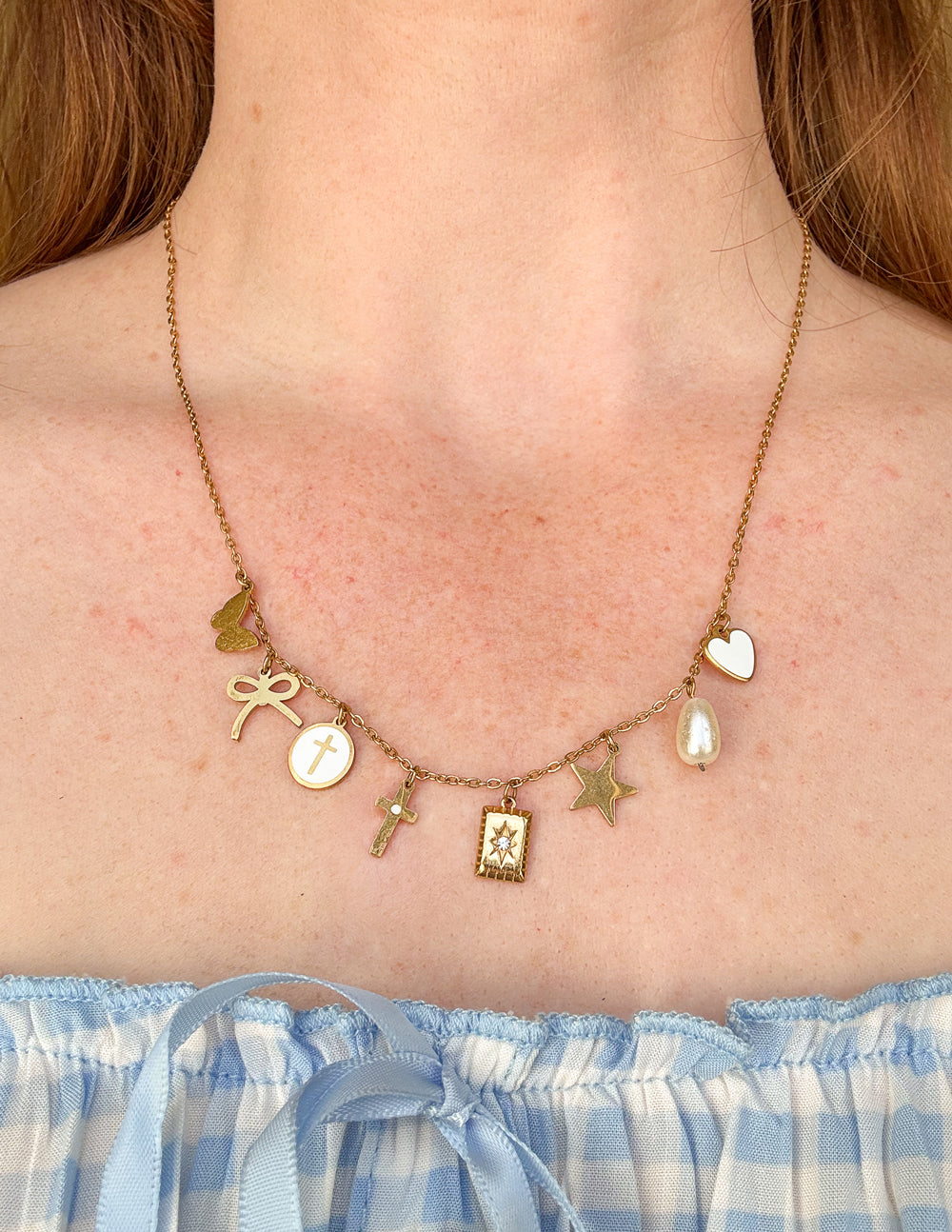 Gold-tone charm necklace on model, featuring heart, star, cross, and pearl-like drop