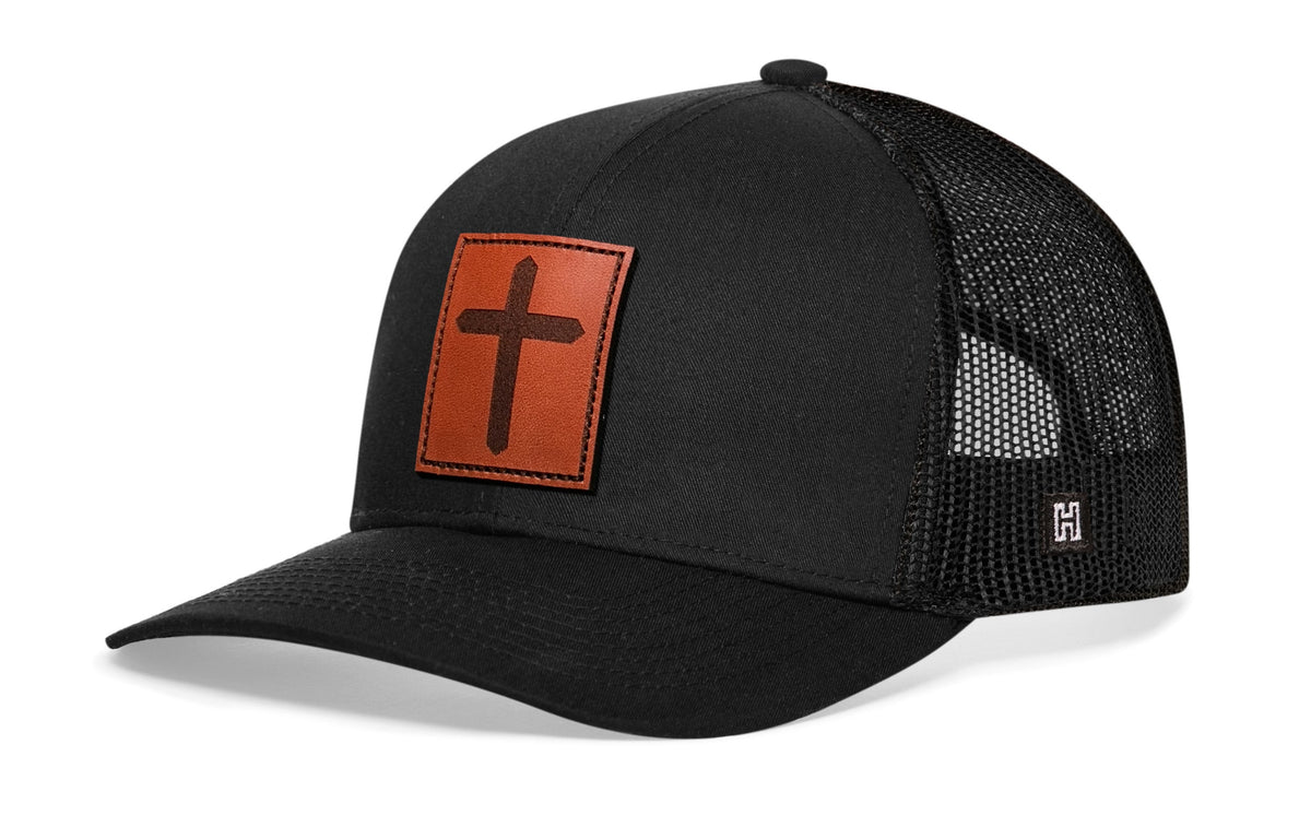 Black leather-look trucker hat with orange cross patch and mesh back