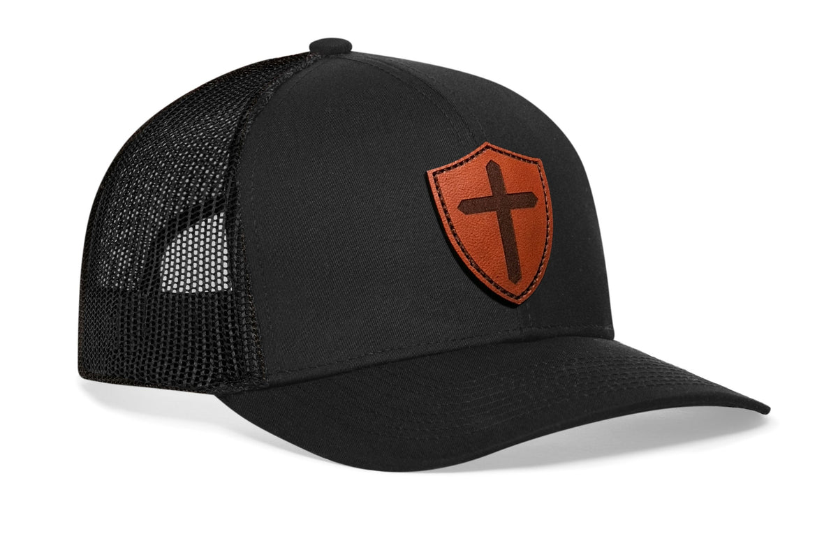Black trucker snapback hat, front orange shield cross patch, mesh back panels.
