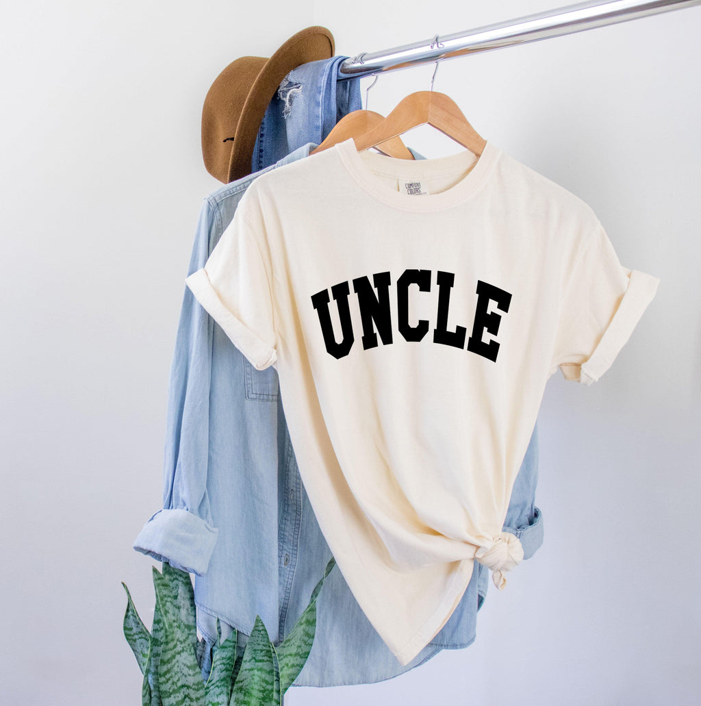Ivory T-shirt with large black “UNCLE” graphic on the chest.
