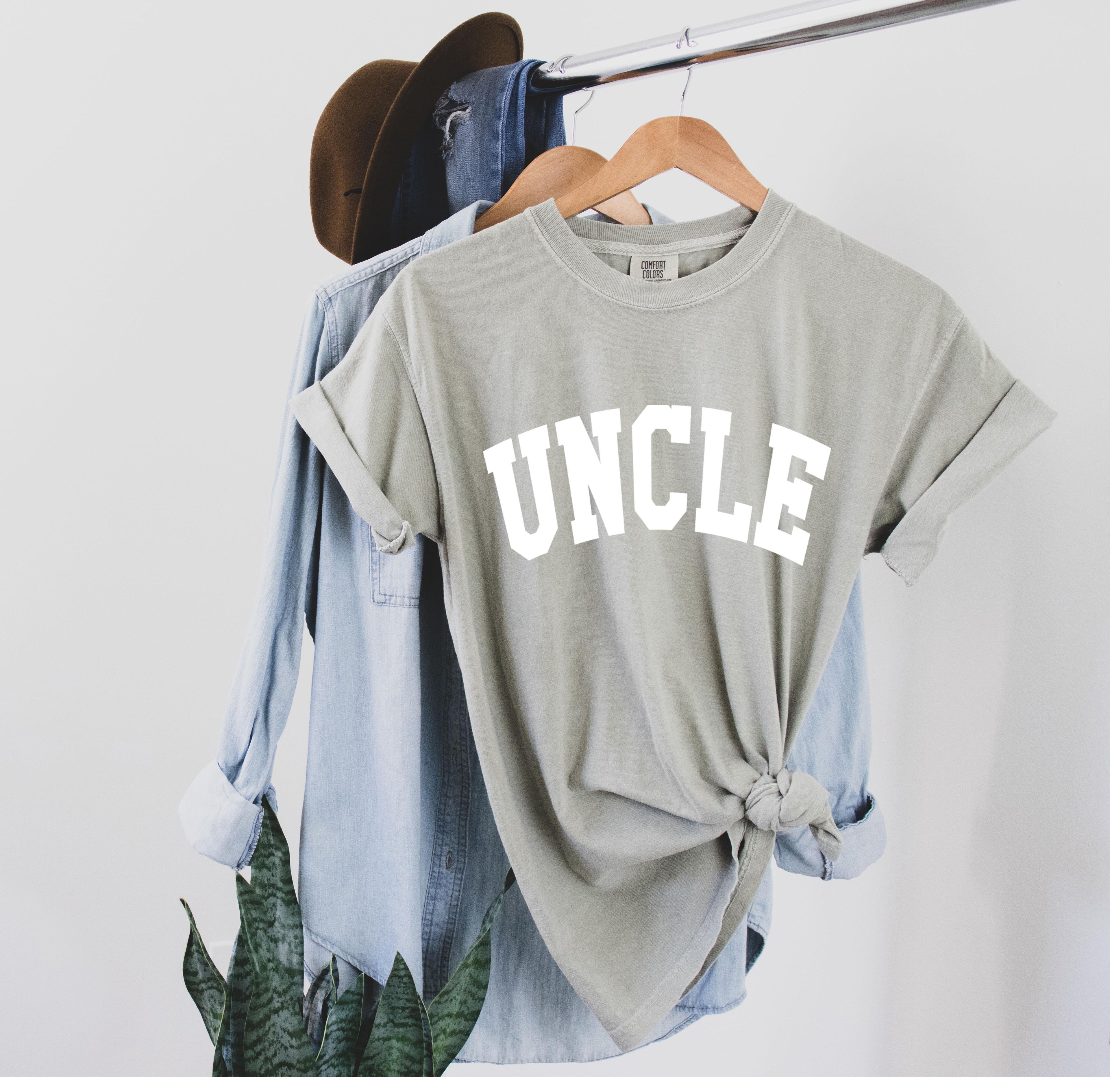 Light gray-green T-shirt with large white “UNCLE” graphic on the chest.