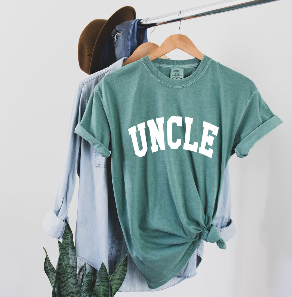 Teal T-shirt with large white “UNCLE” graphic on the chest.
