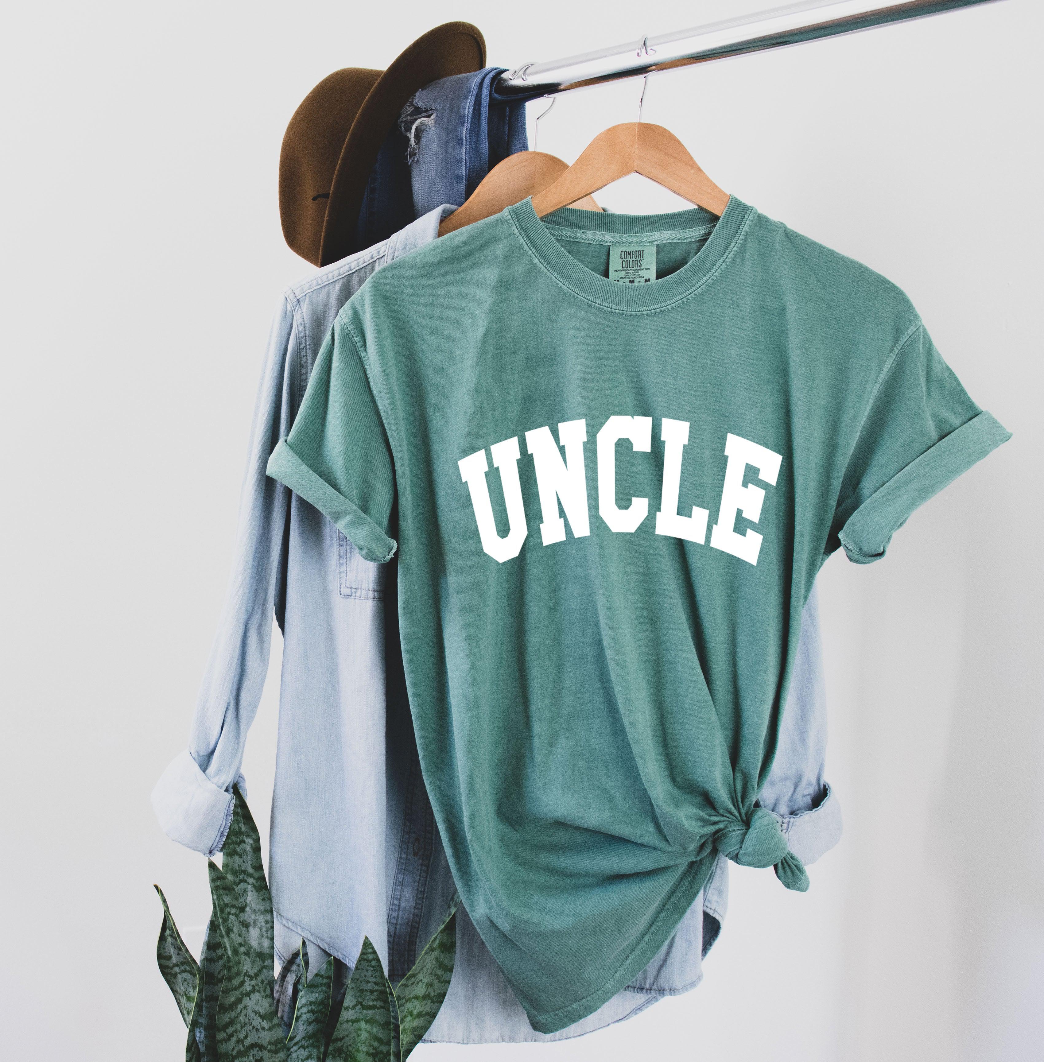 Teal T-shirt with large white “UNCLE” graphic on the chest.